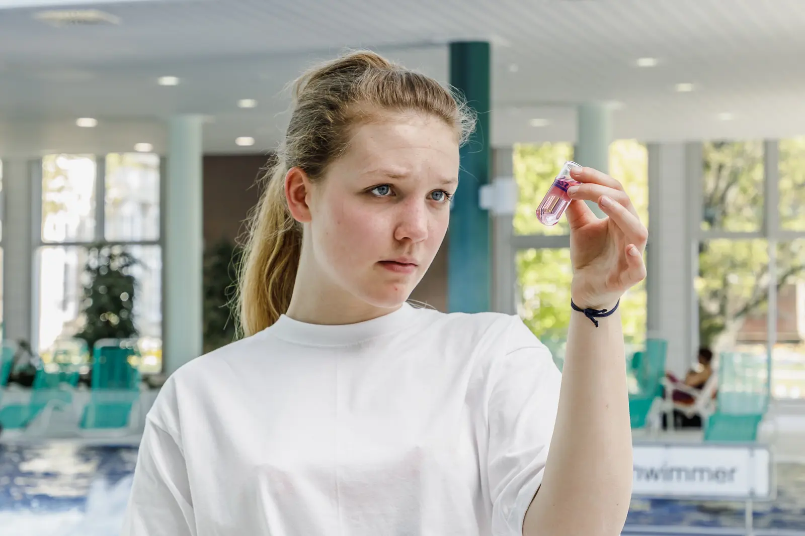 Eine junge Frau schaut eine Wasserprobe in einem Laborglas an.